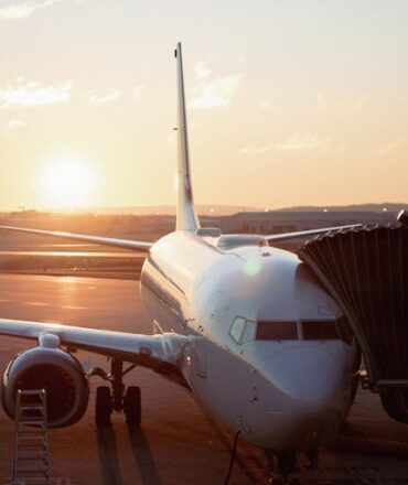 A commercial airplane stands on the tarmac during sunset, ready for boarding at an airport gate.